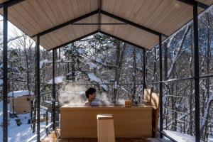 un homme dans un jacuzzi dans une maison de verre dans l'établissement Moving Inn Tokachi Kitanomori, à Taiki