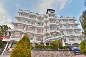 a large white building with a tree in front of it at Hillcrest Resort by DLS Hotels in Shimla