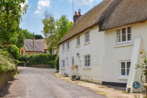 ein altes weißes Haus mit einem Strohdach auf einer Straße in der Unterkunft Martie Cottage - cosy cottage idyllic village in Whitcombe