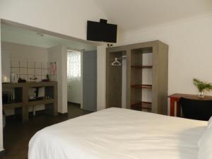 1 dormitorio con cama blanca, escritorio y TV en President Paul Kruger Guest Lodge, en Rustenburg