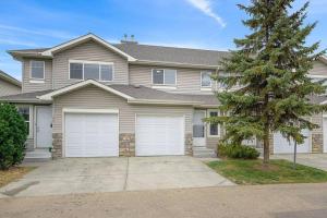 a house with two garage doors and a tree at Large Townhome Near Anthony Henday in Ellerslie with Driveway & Visitor Parking, King Bed, 4 Queen Beds, Fully Equipped Kitchen & More! in Edmonton