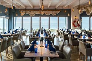 a dining room with tables and chairs with the ocean in the background at StrandResort Markgrafenheide in Warnemünde