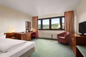 a hotel room with a bed and a desk and a television at Amedia Siegen, Trademark Collection by Wyndham in Siegen