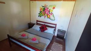 un pequeño dormitorio con una cama y una pintura en la pared en Camping Hostal Tipanie Moana Aeropuerto Centro en Hanga Roa