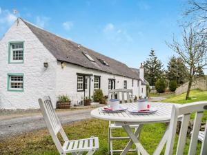 ein Tisch mit zwei Stühlen und ein weißes Haus in der Unterkunft Blackside Cottage in stunning Ayrshire countryside in Mauchline
