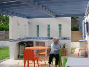 eine ältere Frau, die an einem Tisch auf einer Terrasse mit Stühlen sitzt in der Unterkunft Le zihans in Port-de-Lanne