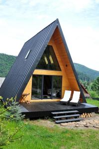 ein kleines Haus mit schwarzem Dach und zwei weißen Stühlen in der Unterkunft Macko’s cabin in Băile Tuşnad