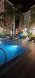 a swimming pool at night with palm trees and buildings at Happy Stays B - End Unit Greenery View at SMDC Hope Residences in Trece Martires