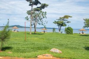 a field with grass and trees and a body of water at Buvuma Island Beach Hotel in Jinja