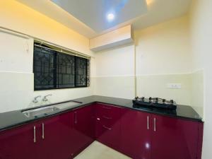 uma cozinha com armários vermelhos, um lavatório e uma janela em AL-Kabeer Heights em Kazhakuttam