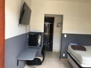 a room with a bed and a desk and a television at Suítes Saraiva in Uberlândia