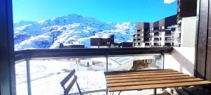 a bench on the balcony of a building with snow covered mountains at STANDING 5 Pax LES MENUIRES in Les Menuires