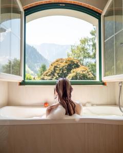 a woman sitting in a bath tub looking out a window at Sylvana's Wohlfühl Hotel in Mayrhofen