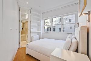 Dormitorio blanco con cama blanca y ventanas en The Mews Apartment In Kensington en Londres