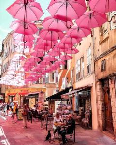 Um monte de guarda-chuvas cor-de-rosa pendurados numa rua. em studio bas de villa, jardin et spa (été seulement) em Le Tignet