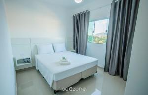 a white bed in a room with a window at Apto 8min do Centro de Poços MBI022 in Poços de Caldas