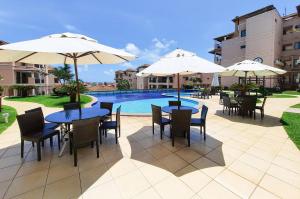 a patio with tables and umbrellas next to a pool at Beverly Hills 2 Suítes Apto Completo 500m Praia in Aquiraz