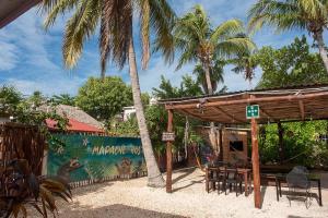 un pabellón con mesas, sillas y palmeras en Mapache Hostel & Camping en Holbox Island