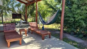 Eine Gruppe von Bänken und eine Hängematte auf einer Terrasse in der Unterkunft La Mora Cabañas in Villa Urquiza