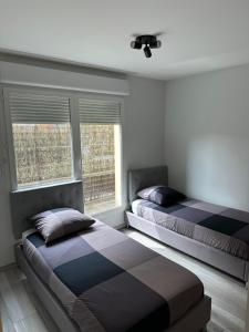 two beds in a bedroom with two windows at Appartement proche Paris et Disney land. in Rosny-sous-Bois