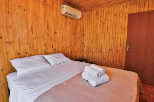 a bed in a wooden room with towels on it at Pousada Refúgio Araçá in Morro Redondo