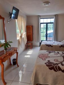 a room with two beds and a desk and a television at HOTEL CAMELINAS AREA BLANCA in Pátzcuaro