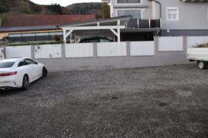 un coche blanco aparcado en un estacionamiento junto a una valla en StayComfy Apartments mit Aussicht auf die Berge, en Proleb