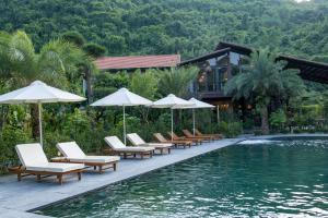 a pool with lounge chairs and umbrellas next to a resort at Tam Coc Retreat Ninh Binh in Ninh Binh