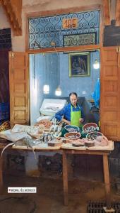 Hostel riad Dar lala sofia في فاس: رجل ذو مريلة خضراء يجلس على طاولة مع الطعام