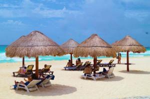 een groep mensen zittend in stoelen onder parasols op een strand bij Solymar hermoso apartamento in Cancun