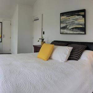 a white bed with a yellow pillow on it at Abbeygate Cottage in Auckland
