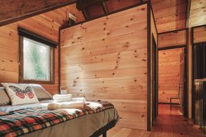 Dormitorio en cabaña de madera con cama y ventana en Le Refuge, en Saint-Henri-de-Taillon