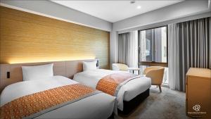 松山市にあるダイワロイネットホテル松山のベッド2台と窓が備わるホテルルームです。