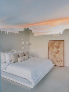 a bedroom with a white bed with a painting on the wall at MAJA Canggu in Canggu