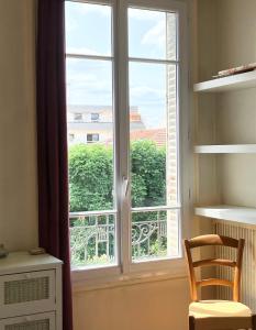 uma janela num quarto com uma cadeira ao lado em Charmant appartement 1930 Centre-ville Nogent-sur-Marne em Nogent-sur-Marne