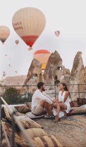 Ein Mann und eine Frau sitzen auf einem Felsen mit Heißluftballons in der Unterkunft Castle Cave Hotel in Goreme