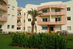 an apartment building with a palm tree and flowers at MOHAMMEDIA 55 in Mohammedia