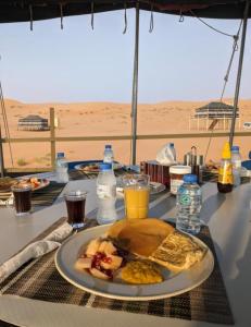 einen Tisch mit einem Teller mit Frühstückslebensmitteln und Getränken in der Unterkunft Hamood desert local camp in Al Wāşil