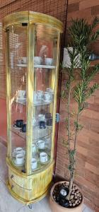 a glass cabinet with dishes in it next to a plant at CASA DA ZEZÉ Pousada & Hotel ITABORAÍ in Itaboraí