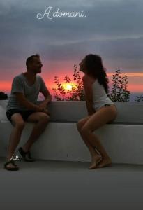 Um homem e uma mulher sentados num parapeito a ver o pôr-do-sol. em Casa al tramonto...sunset lovers retreat em Lipari