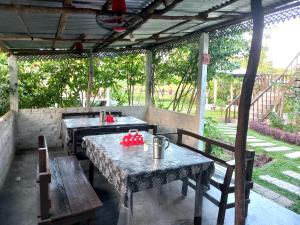 eine Außenterrasse mit Tischen, Bänken und Bäumen in der Unterkunft Oronner Din Ratri in Sreemangal