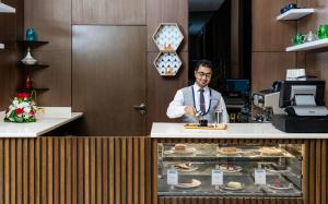 فندق جايدن-Jayden Hotel في المدينة المنورة: رجل يقف خلف مكتب مع طبق من الطعام