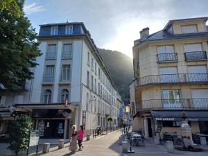 dos personas caminando por una calle de la ciudad con edificios en Studio hyper centre lumineux et fonctionnel Luchon, en Luchon