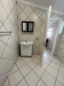 ein weiß gefliestes Bad mit einem Waschbecken und einem Spiegel in der Unterkunft 9 wena Ave Guesthouse in Klerksdorp