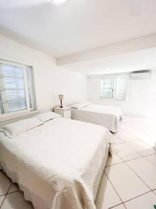 two beds in a white room with two windows at Paraíso de luxo: sua casa dos sonhos in Angra dos Reis