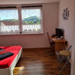 a bedroom with a bed and a desk and two windows at Wilhelm Busch Stube in Ebergötzen