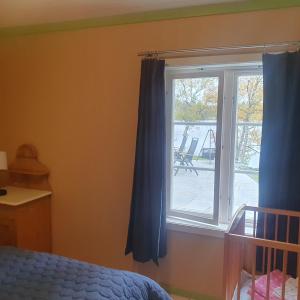 a bedroom with a window with blue curtains and a crib at Brekkveien 81-meget sentral hytte,15 min å gå til Røros sentrum in Røros