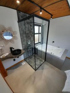 a bathroom with a glass shower and a tub at Pousada Kirana in Praia do Rosa