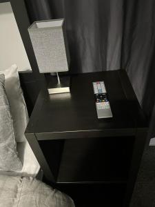 a black nightstand with a lamp and a remote control on it at OAKhouse studio 76 in Kent