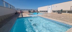 a swimming pool with blue water in front of a building at Wave Itapoã 702 Sul - Praia de Itapoã - Beverly Hills, comércio, piscinas panorâmicas, minimercado e lavanderia in Vila Velha